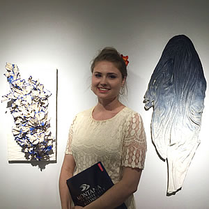 Female student posing in the gallery with her art work