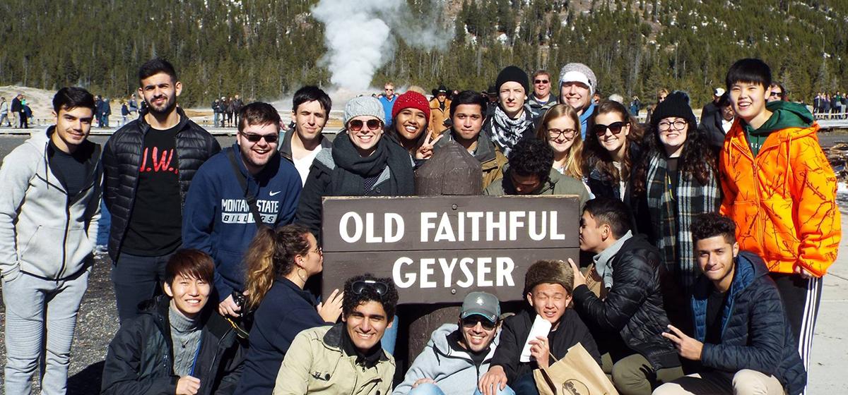 A group of students pose in front of the Old Faithful Geyser