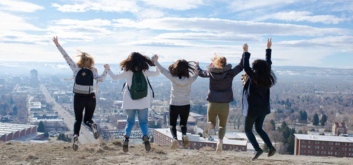 A group of students overlooking Billings jump in unison.