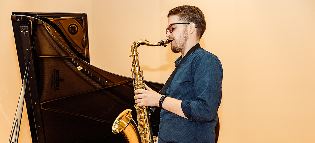 Man with a saxophone next to a piano.