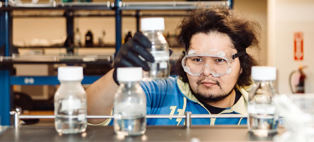 student wearing safety goggles analyzes a lidded glass bottle