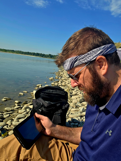 John M. looking at a phone lakeside