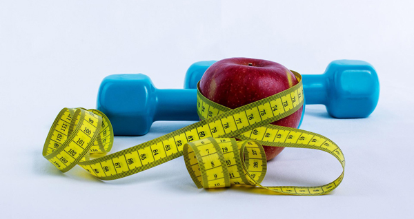 an apple wrapped with a measuring tape next to a dumbbell