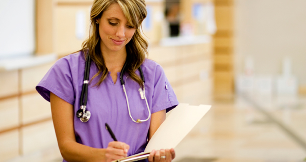 woman in scrubs and wearing a stethescope writes in chart