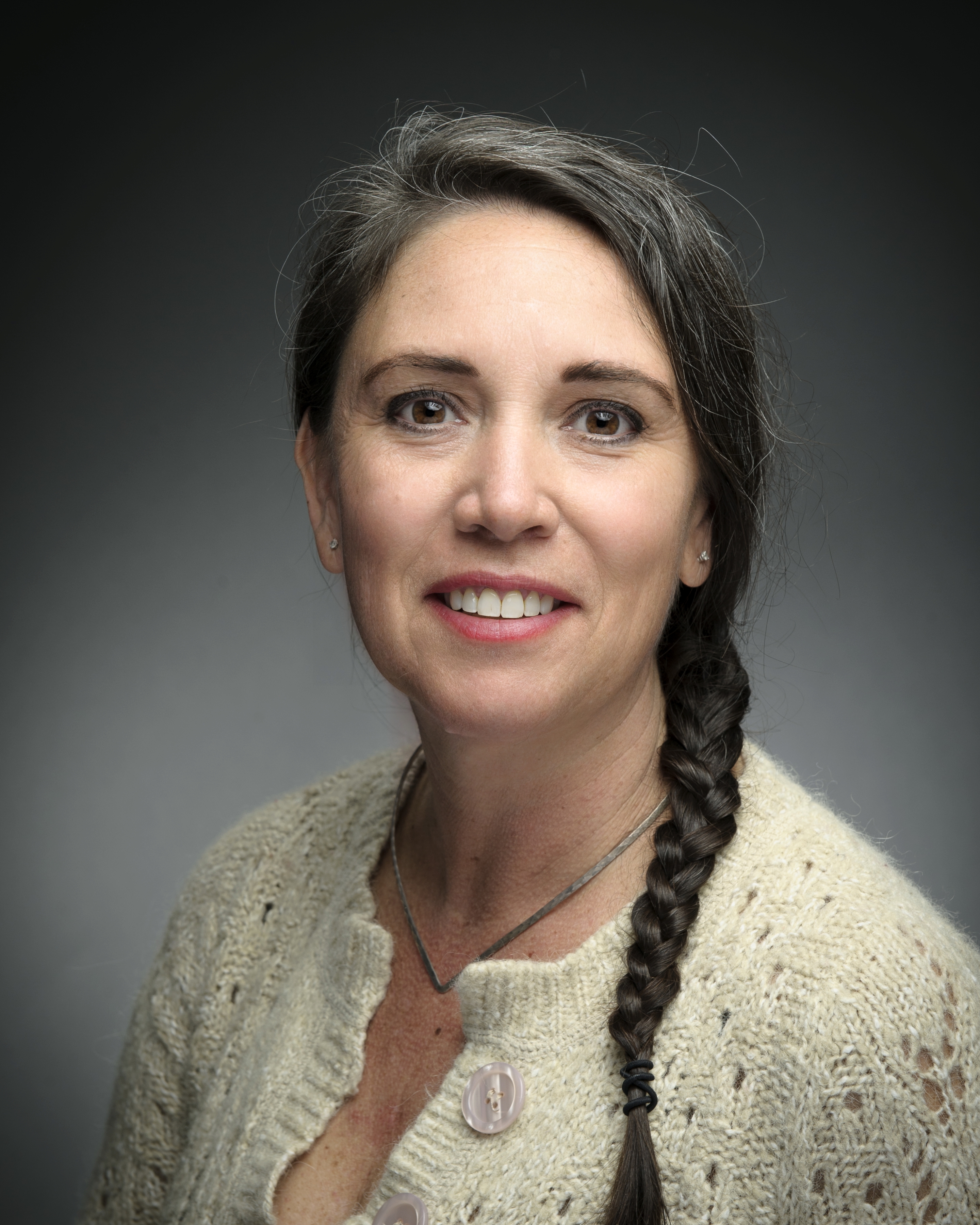 A smiling women with a long, dark braid and wearing a cream-colored blouse.
