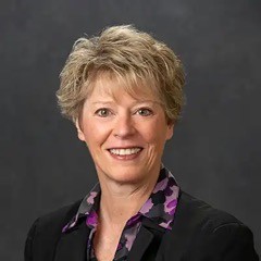 A smiling women with a blond bob and a colorful black-and-purple blazer.