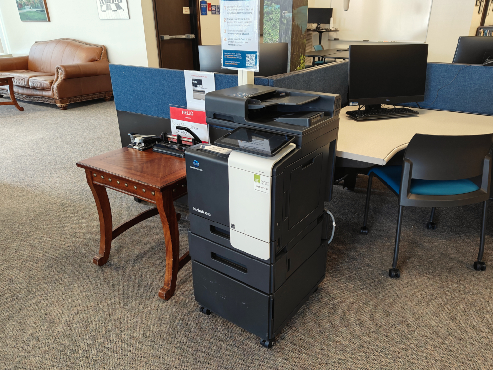 A printer surrounded by blue and red chairs.