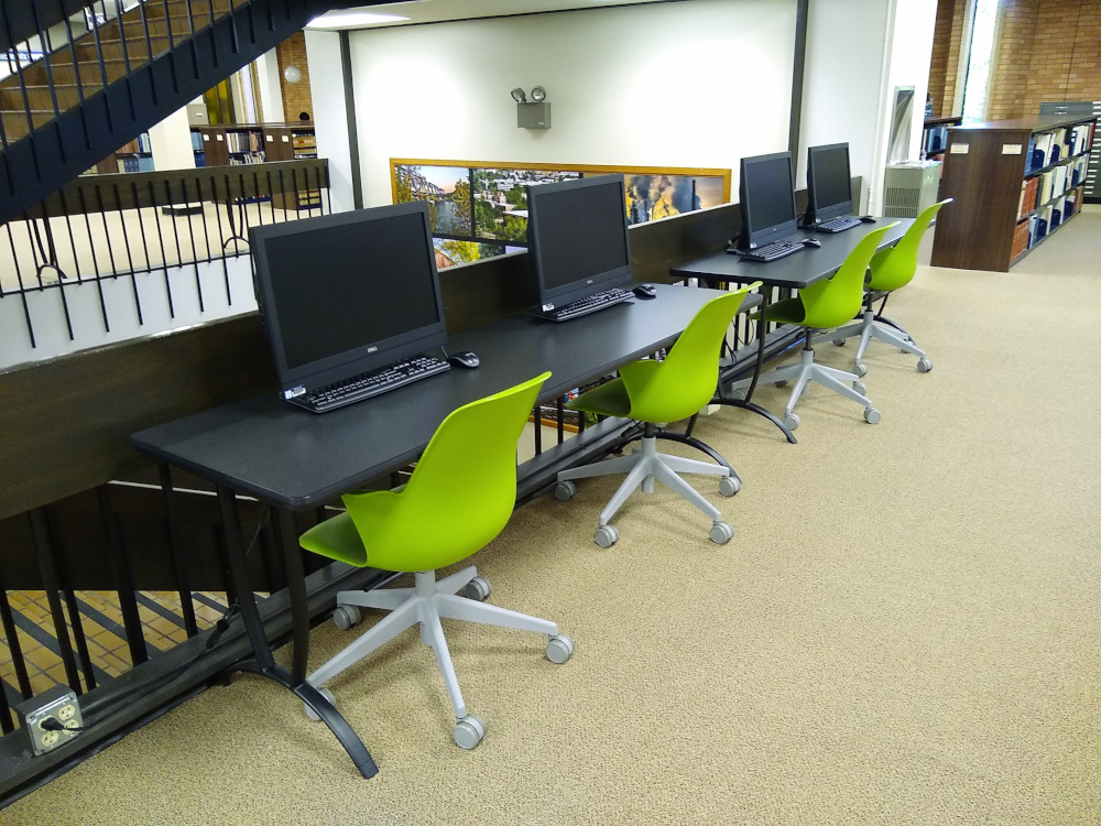 4 computer stations with green chairs lined against a stairwell railing.