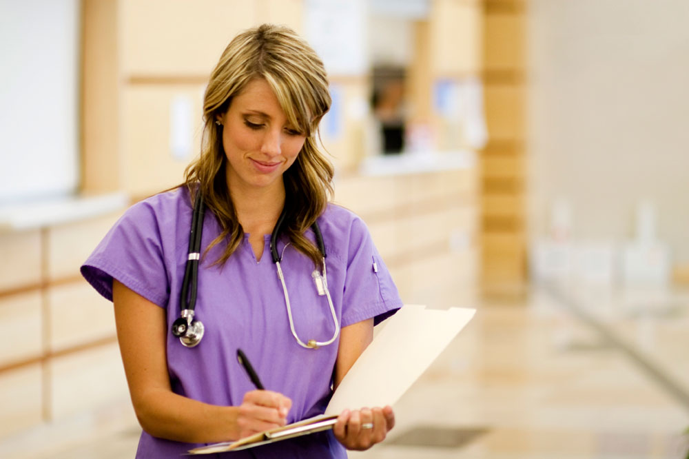 nurse in scrubs writing on a clipboard